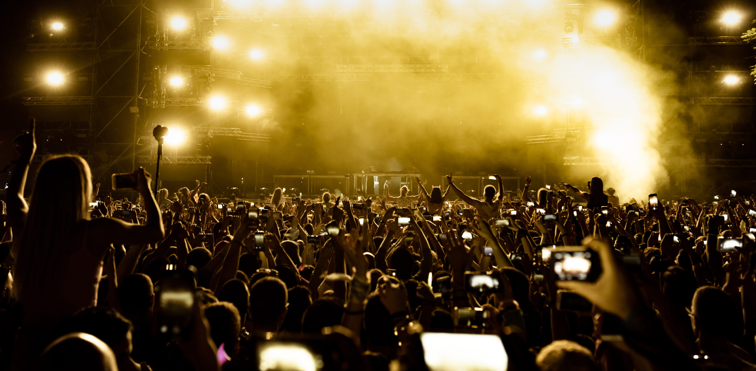 Rear view of excited fans having fun at music festival and taking pictures of stage with their smart phones.  Copy space.